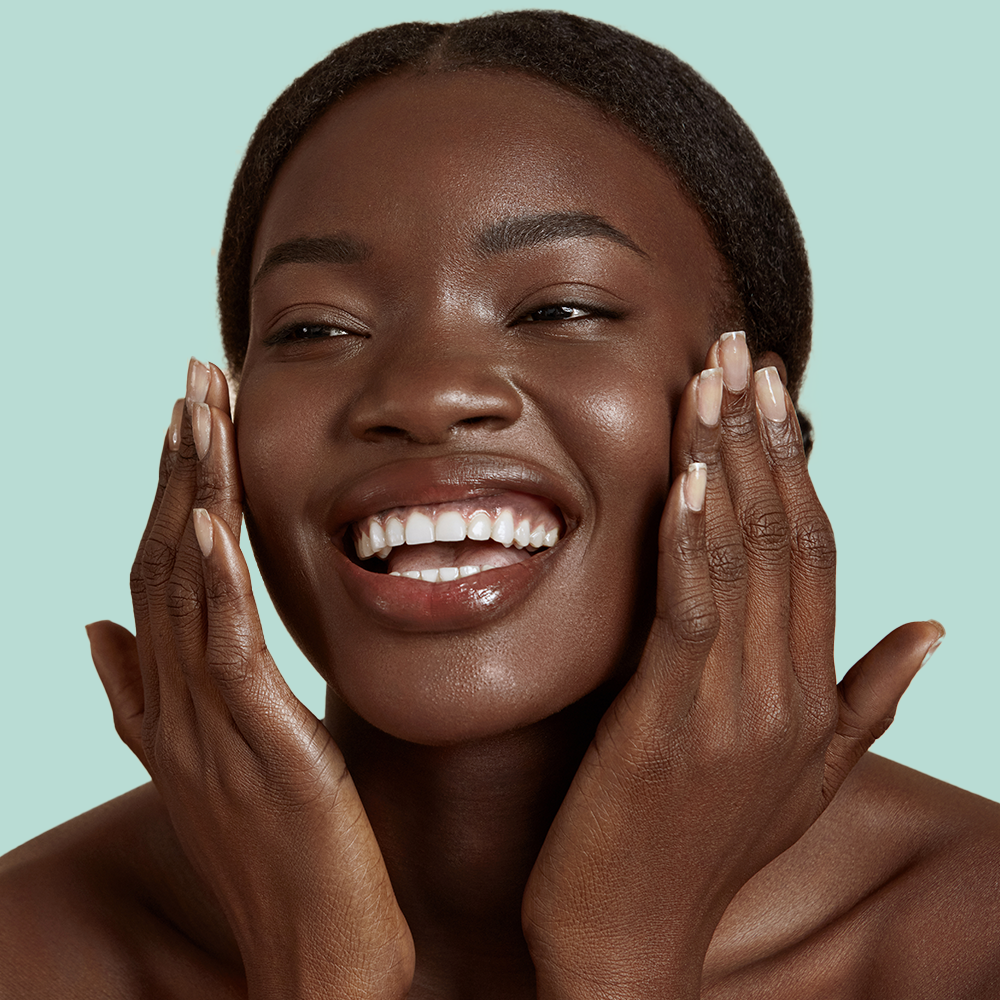 Smiling person touching face against green background.