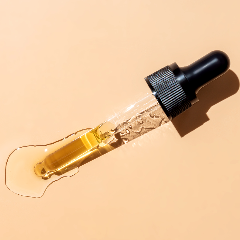 Dropper with oil on peach background.