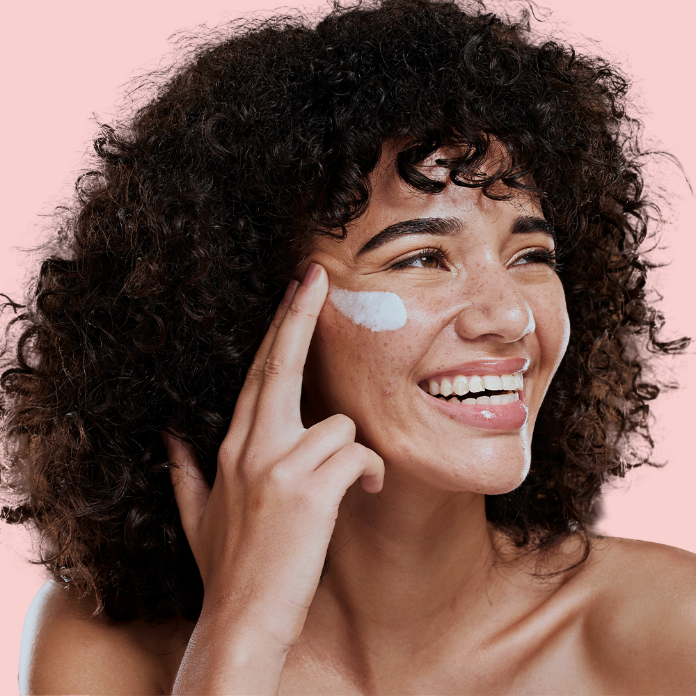 Smiling woman applying cream on face.